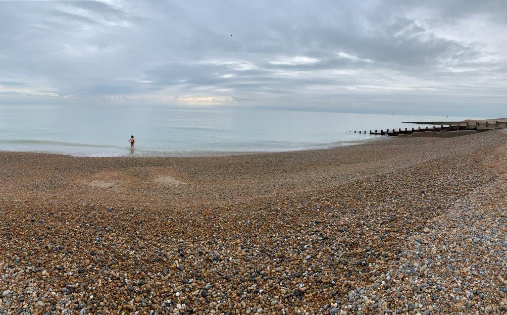 Quiet shingle beach at low tide with a lone swimmer entering the sea